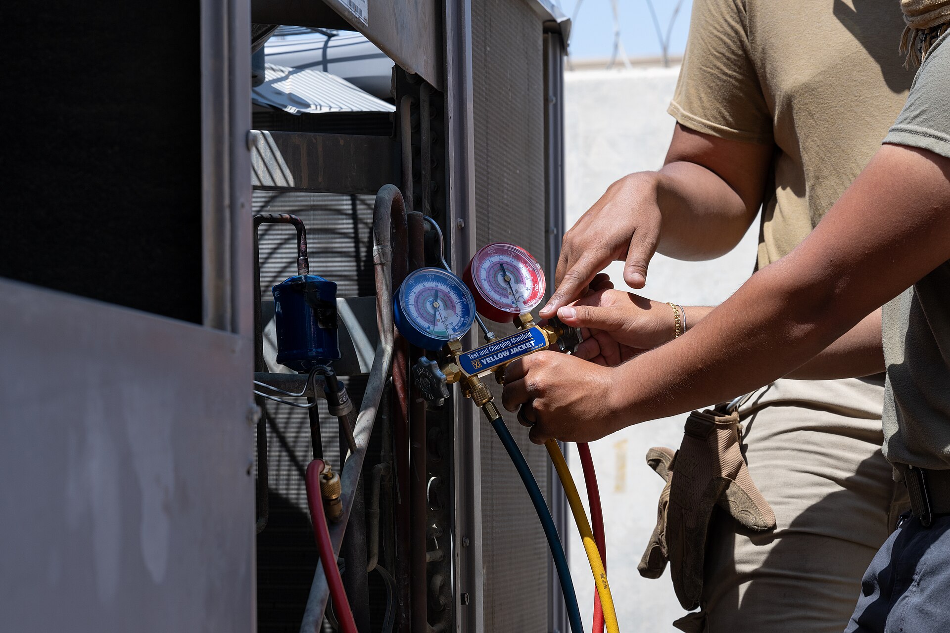 HVAC technicians using a pressure gauge to diagnose an air-conditioning unit
